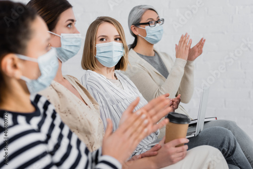 multiethnic businesswomen in medical masks applauding during seminar in meeting room