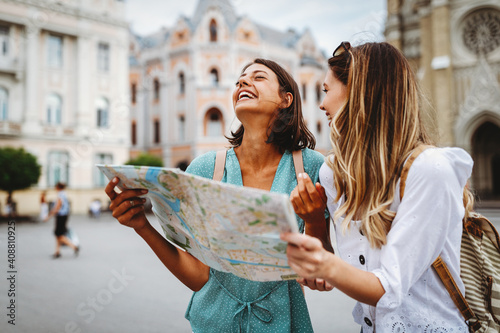 Fun, friends, travel and tourism concept. Beautiful girls looking for direction in the city photo