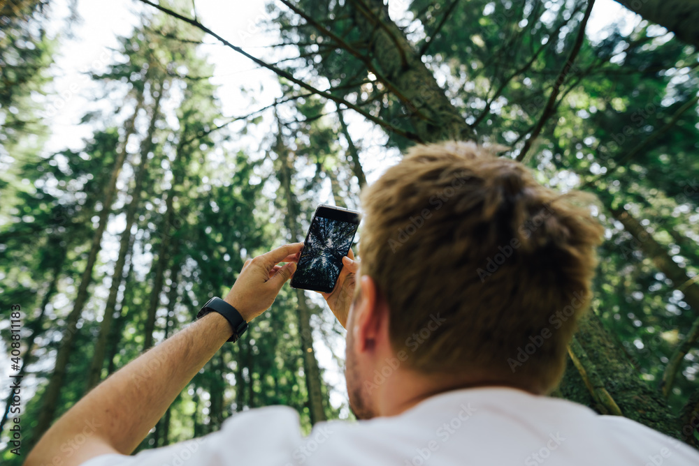 Man shoots trees and sky in the forest on a smartphone camera on a hike. Guy makes photo content in the mountain forest for social networks. Man shoots trees and sky in the forest on a smartphone camera on a hike. Guy makes photo content in the mountain forest for social networks.