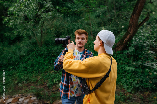 Two male video makers create videos in nature, a guy holds a camera on a stabilizer and communicates with a colleague. Friends shoot travel videos on vacation on a hike. Creating video content. © bodnarphoto