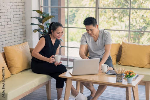 Asian man and woman family in casual outfit sitting in living room drinking coffee and using laptop together in happy and smile emotion © Supagrit Ninkaesorn