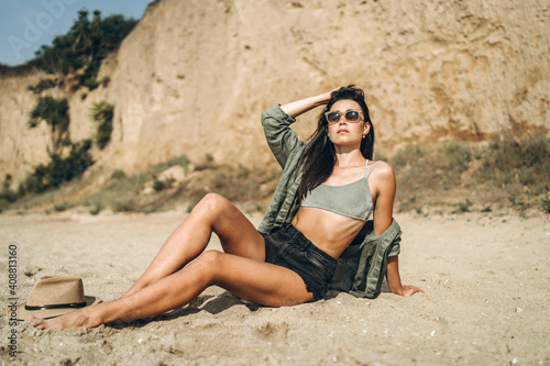 Brunette girl in hat relaxing on the beach with rocks on background.