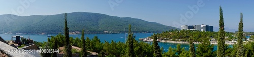 Panorama picture of scenery view in the sunny day. Beautiful blue sky, islands, green mountain, boats and fresh ocean on the beach. Cypress in the foreground. Summer vacation concept.