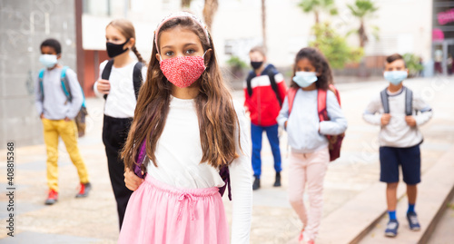 Portrait of tween schoolgirl in protective face mask with rucksack on her way to college on warm fall day. Back to school after lockdown concept.