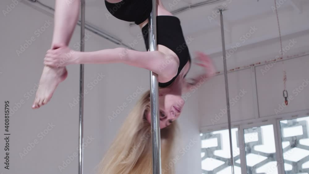 Pole dancing - blonde woman spinning on the dancing pole upside down holding her ankle