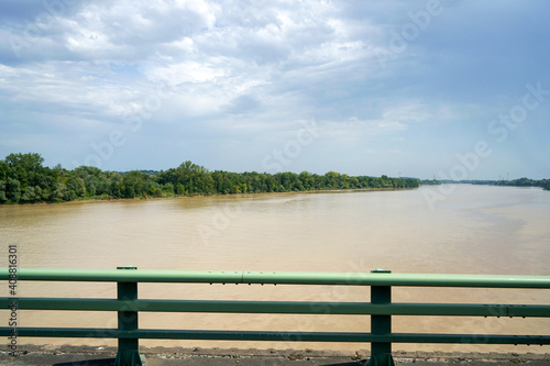 View of dirty colored-floodwaters flowing downstream in a river under a bridge