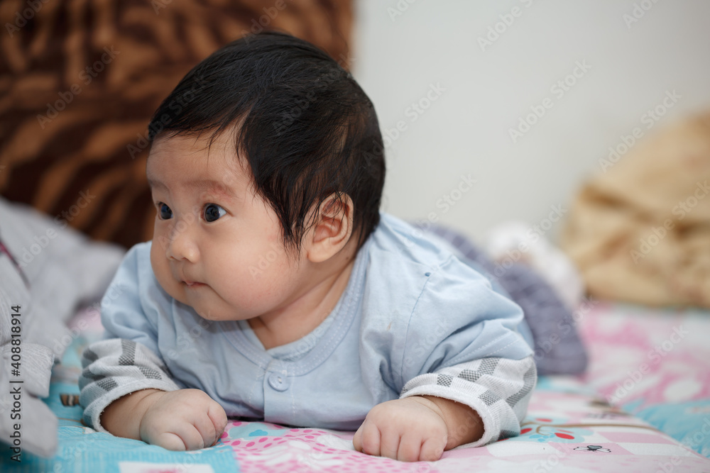 Asian infant boy lying on her stomach on bed learning to crawl Asian infant boy lying on her stomach on bed learning to crawl