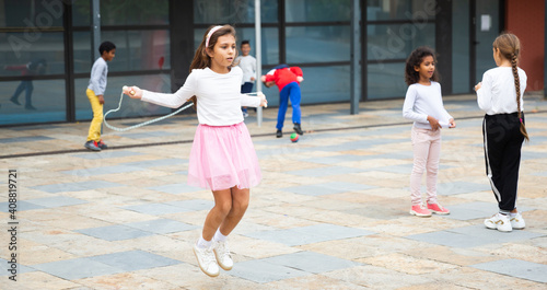 Happy carefree tweenager girl enjoying break between lessons, skipping rope in schoolyard