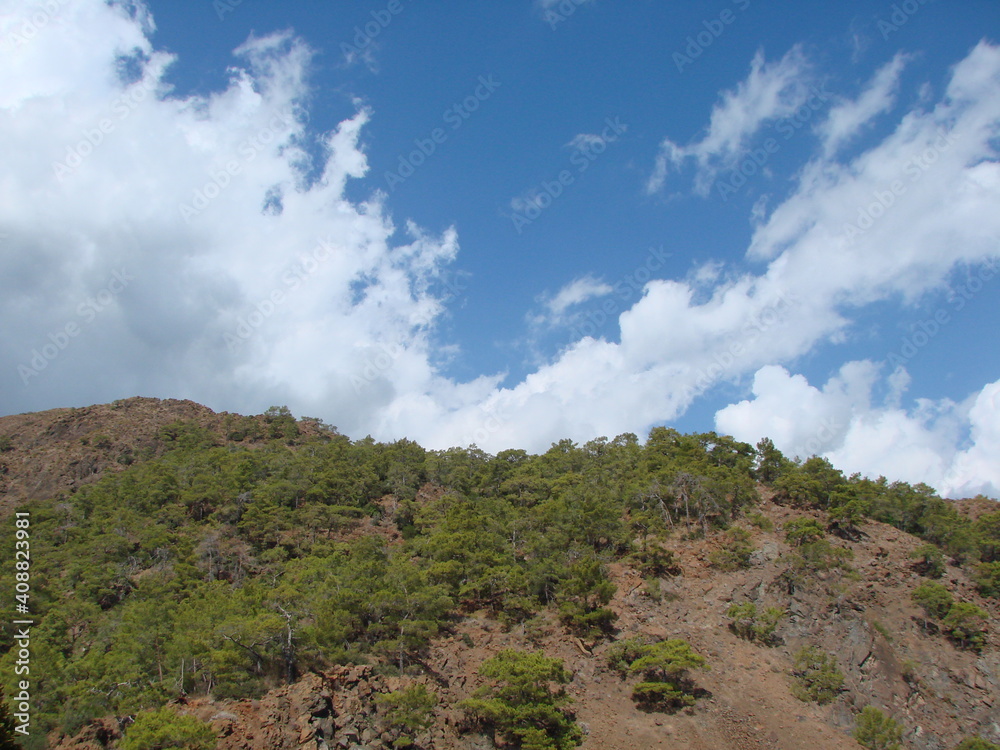 Panorama of the blue sky, which is approached by a large white cloud and almost covers the top of the mountain range.