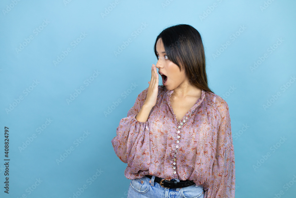 Beautiful latin woman wearing a pink shirt over blue isolated background covering mouth with hand, shocked and afraid for mistake. surprised expression Beautiful latin woman wearing a pink shirt over blue isolated background covering mouth with hand, shocked and afraid for mistake. surprised expression