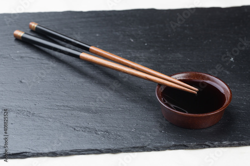 .Black board on a white background. Empty black granite stone rectangular board on white textured background. sushi sticks and soy sauce on coasters on a stone board