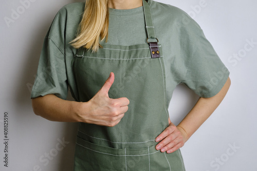 A woman in a kitchen apron. Chef work in the cuisine. Cook in uniform, protection apparel. Job in food service. Professional culinary. Green fabric apron, casual clothing. Handsome baker posing