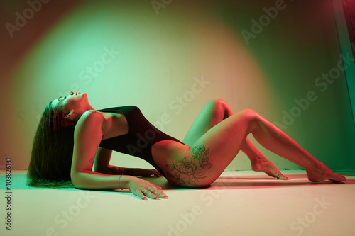 Portrait of a tattoo woman wearing in a black bodysuit lying on the studio floor.