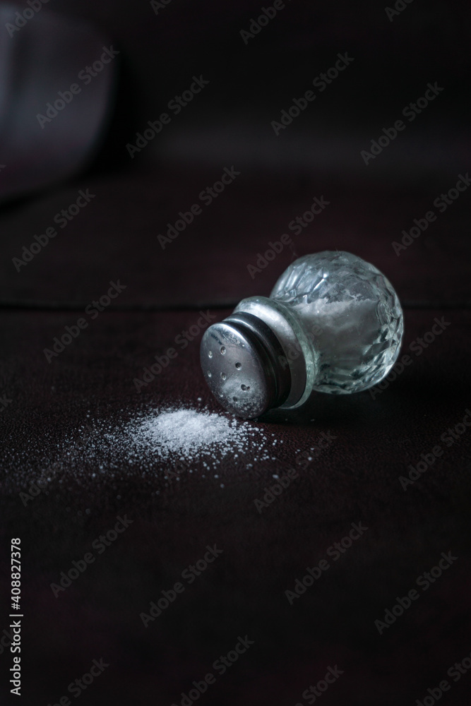 glass jar spilling salt on a leather-like textured surface glass jar spilling salt on a leather-like textured surface