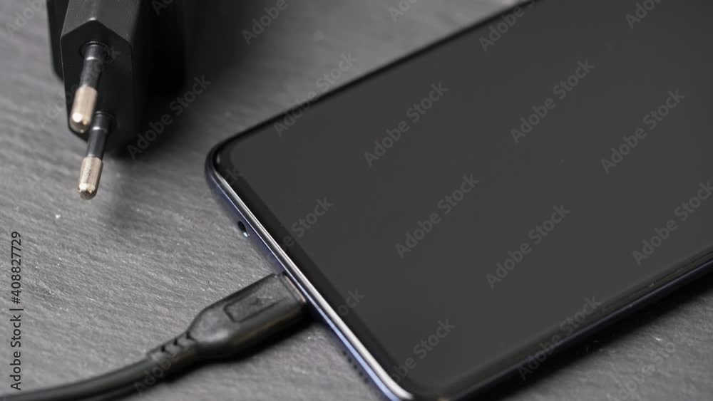 Rotating close-up of charger plugged into turned off smartphone on grey surface. Rotating close-up of charger plugged into turned off smartphone on grey surface.