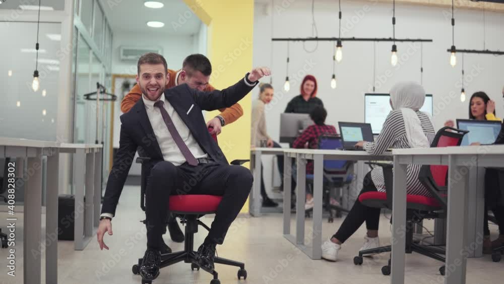 Young businessman in smart suit play chair pushing race with multicultural collages in coworking startup offfice. multiethnic developers at work background Young businessman in smart suit play chair pushing race with multicultural collages in coworking startup offfice. multiethnic developers at work background
