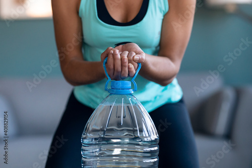 Afro beautiful gymnast woman doing exercices lifting eight liters water bottles in living room at home. photo
