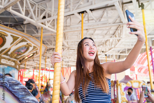 Young pretty woman taking selfie on carousel in amusement park. Attractive women taking selfie in amusement park.