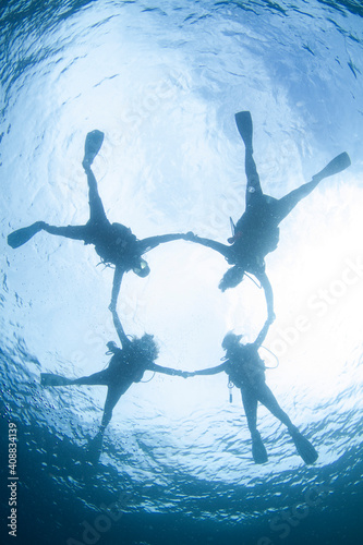 Four silhouettes of Scuba Divers swimming circle position over the ocean sun above at tropical water komodo National Park, Indonesia.