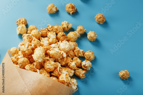Popcorn in caramel glaze in a paper envelope on a blue background.