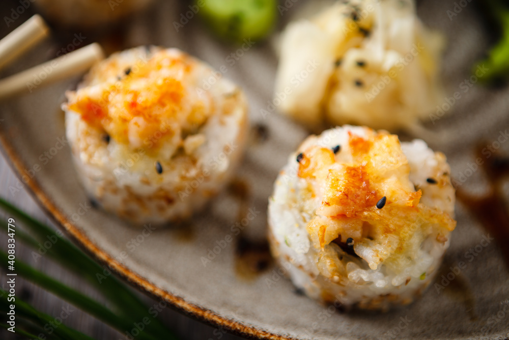 Baked sushi maki rolls with prawns and crab on a plate with chopsticks, soy sauce, wasabi and ginger. Japanese traditional fish food closeup served for lunch in modern gourmet restaurant Baked sushi maki rolls with prawns and crab on a plate with chopsticks, soy sauce, wasabi and ginger. Japanese traditional fish food closeup served for lunch in modern gourmet restaurant