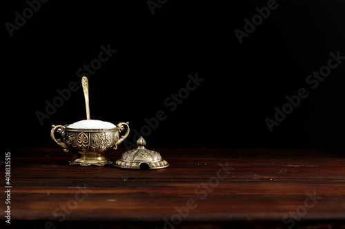 White sugar in an exclusive sugar bowl on a wooden table in an atmospheric dark kitchen 
