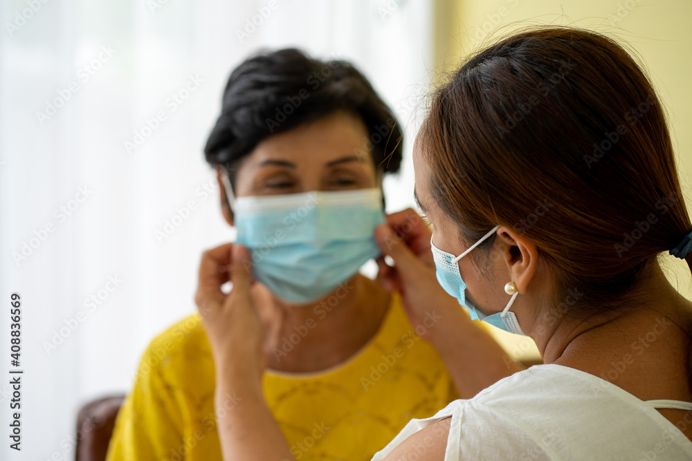 Asian old senior sick woman wearing protective face mask sitting in hospital with daughter taking care helping 