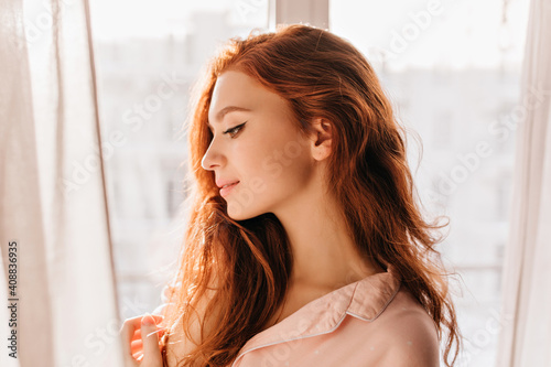 Romantic long-haired lady posing at home. Portrait of pensive attractive ginger girl.