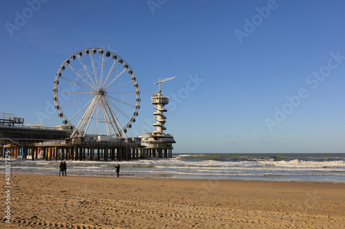 Ferris wheel on De Pier in The Hague Scheveningen on a windy winter day with blue sky and people at the beach, the Netherlands, Europe © tselykh