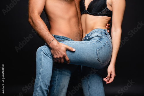 partial view of shirtless man embracing woman in jeans and touching her leg on black