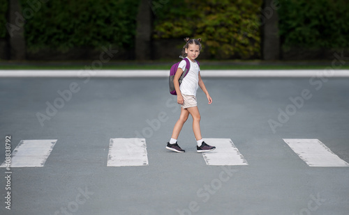 Schoolgirl crossing road on way to school. Zebra traffic walk way in the city. Concept pedestrians passing a crosswalk. Stylish young teen girl walking with backpack. Active child