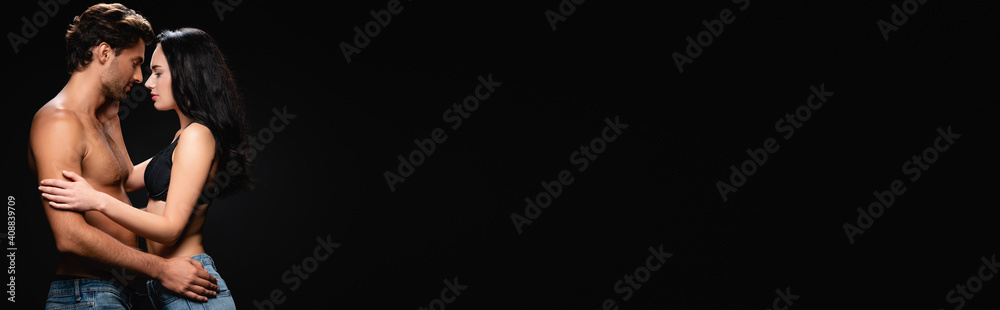 side view of shirtless man and woman in bra embracing face to face isolated on black, banner side view of shirtless man and woman in bra embracing face to face isolated on black, banner