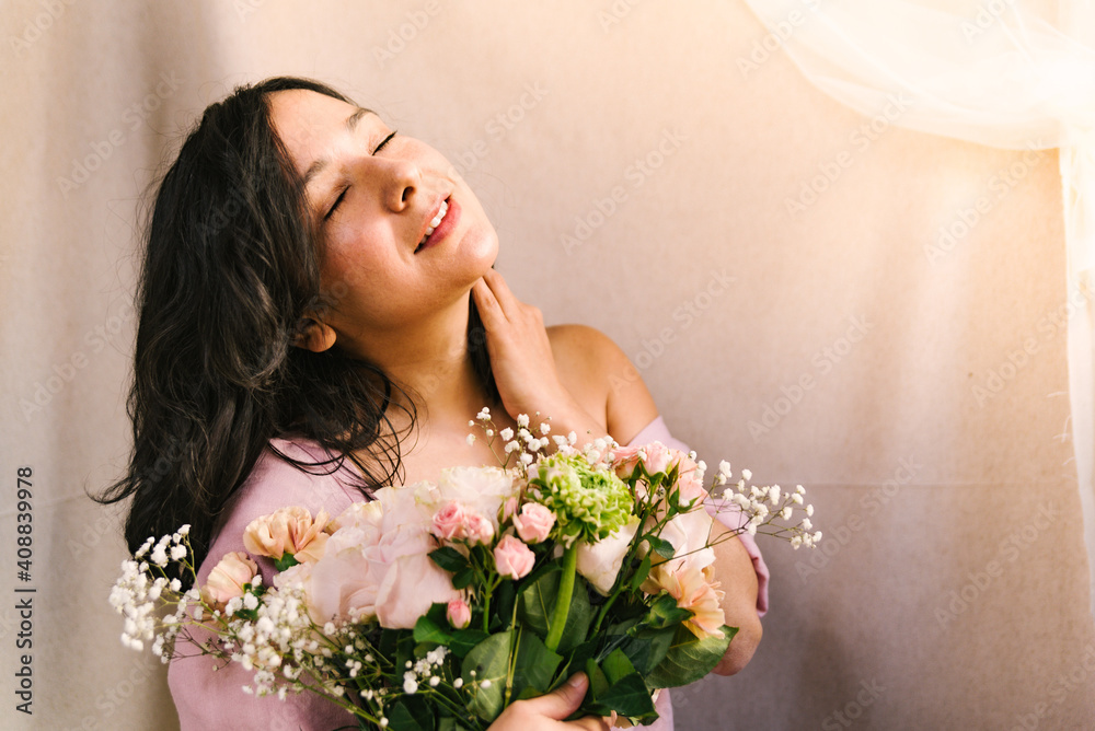 attractive young woman enjoying and feeling the sun holding a flowers bouquet with simple pink dress. Smiling and confident woman during spring.