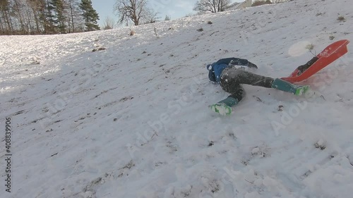 A boy sledging has a wipeout and falls off his sledge into the fresh snow