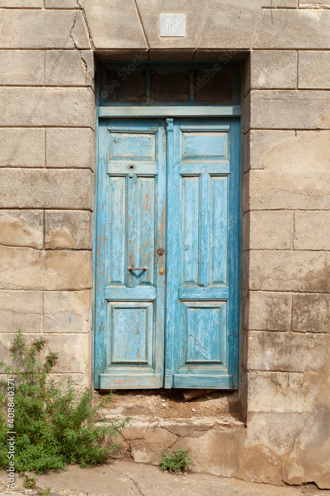 An old wooden door, fragile and discolored, painted blue, in a lost street in the outskirts of the city of Huesca, Aragon, Spain.