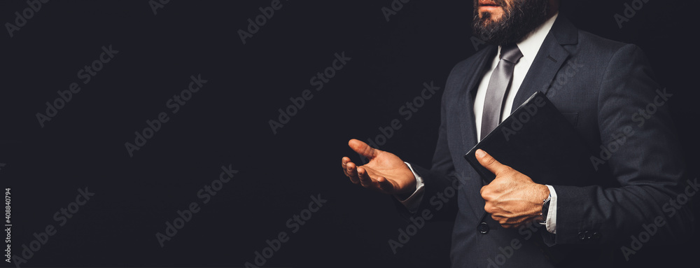 man in suit holding a bible in his arm speaking to another person on a black background - obrazy, fototapety, plakaty 