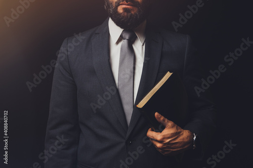 man in suit holding a bible in his arm on a black background photo