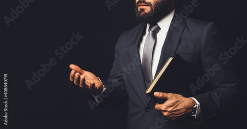 man in suit holding a bible in his arm speaking to another person on a black background