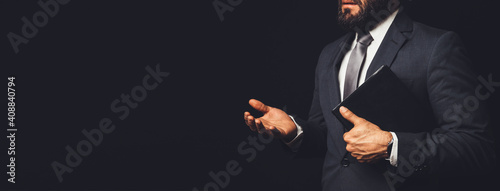 man in suit holding a bible in his arm speaking to another person on a black background photo