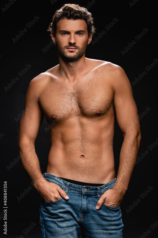 muscular confident man posing with hands in pockets while looking at camera on black background muscular confident man posing with hands in pockets while looking at camera on black background