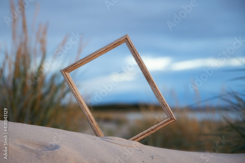 Vintage photo frame on the sand. Summer beach and evening sky background. Empty wooden picture frame. 