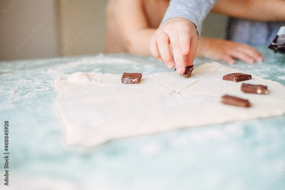 Child's hand placing pieces of chocolate on dough with flour around it Child's hand placing pieces of chocolate on dough with flour around it