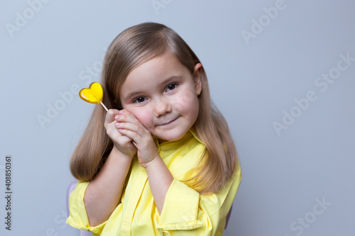 White girl 4 years old holding a yellow lollipop. Grey background.Donation,heart health,world heart day, world health day,world mental health day.