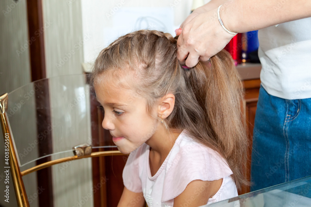Mother combs her daughter hair and braids it at home Mother combs her daughter hair and braids it at home
