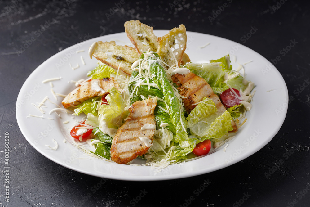 Caesar salad with chicken on a dark background.