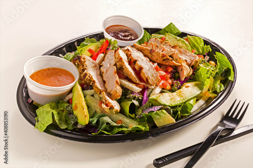 Carry-out grilled chicken salad with avocado in a plastic container on a white surface; copy space