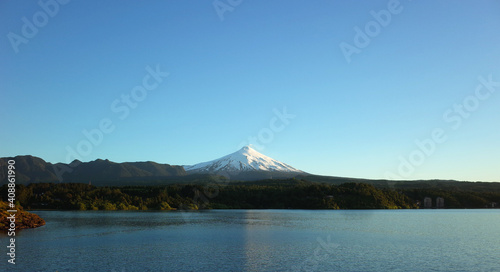 Nature of Chile, Beautiful panoramic landscape, lake Villarrica and snow capped Villarrica volcano under blue sky evning light. Pucon