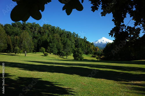 Nature of Chile. Beautiful landscape, sun and shadow, Green grass and forest on hill, Snowy cone of Villarrica volcano under blue sky in sunny day. Green environment, Pucon photo