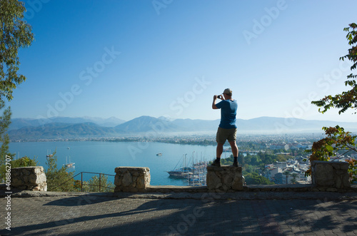 View point on Fethiye town, harbour with turquoise water and mountains, Man tourist taking photo of beautiful Turkish seaside. Blue sky sunny day