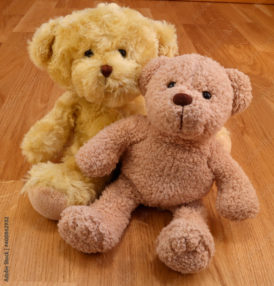 Two cute stuffed teddy bears. Softly smiling kindly. Close up and isolated against a wooden background.